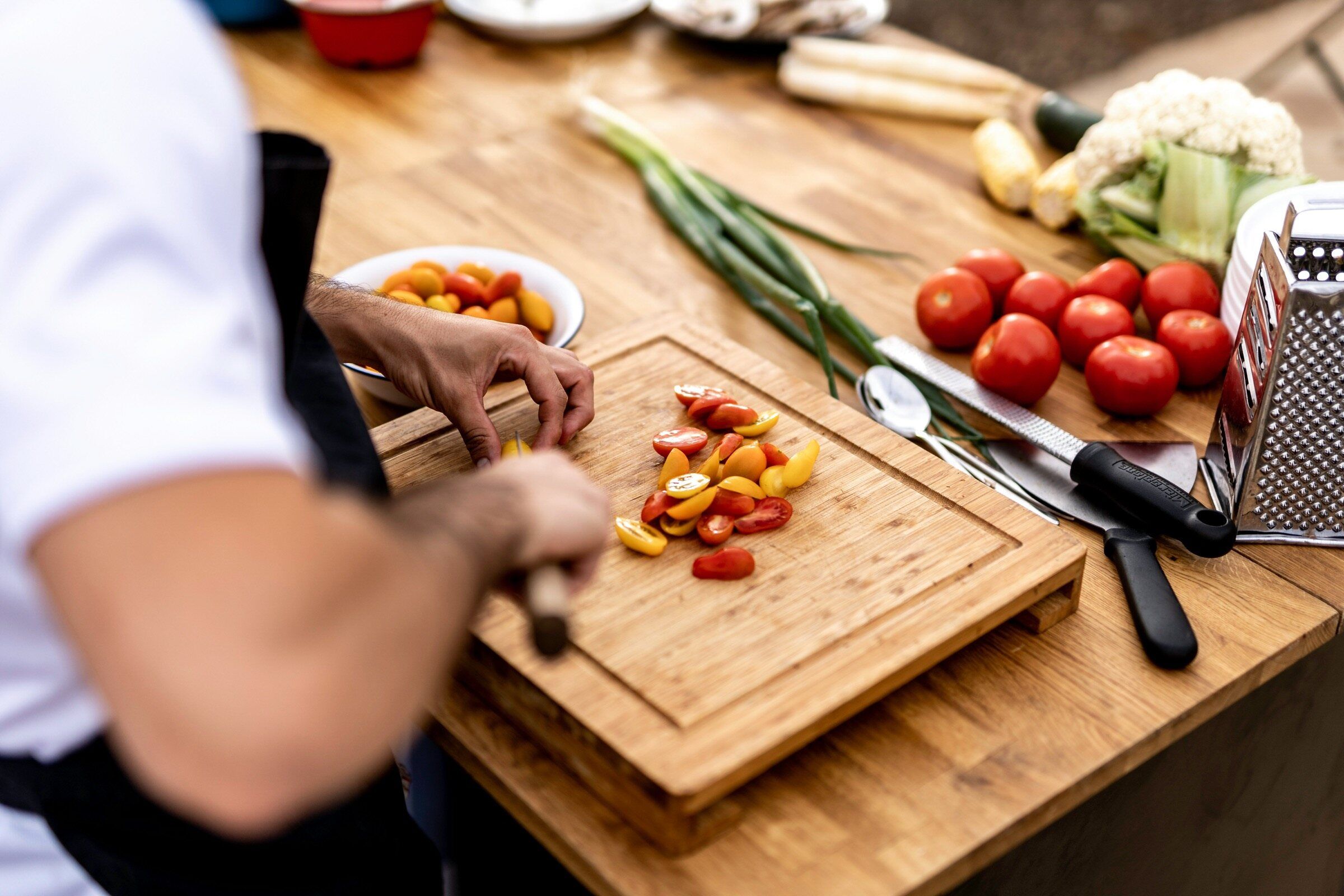 Hands slicing tomatoes on a chopping board in a kitchen