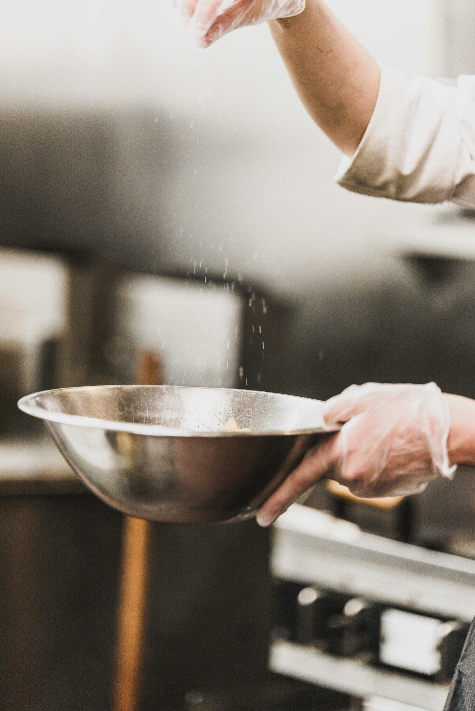 Gloved hands working over a steel bowl in a kitchen