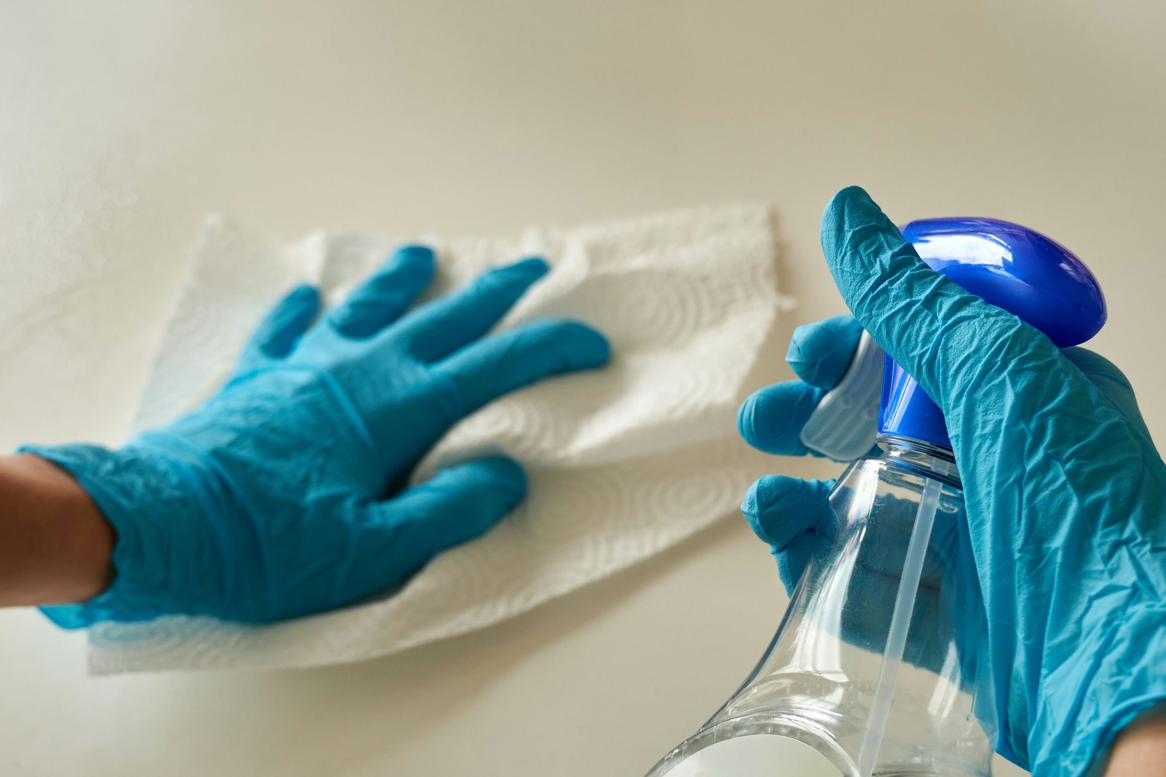 Gloved hands wiping down a bench with a spray and paper towel.